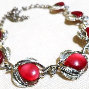 May include: A silver bracelet with red gemstone accents. The bracelet features a delicate design with leaves and swirls. The gemstones are oval-shaped and have a glossy finish.