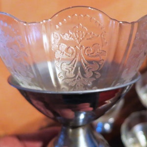 Puede incluir: Un cuenco de vidrio transparente con una base plateada y un patrón grabado decorativo. El cuenco está diseñado para servir postres o aperitivos.