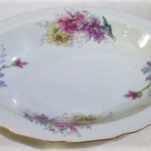 May include: Oval-shaped, white porcelain serving dish with gold trim and handles. The dish is decorated with floral patterns in shades of pink, purple, and yellow. The handles have an ornate design.