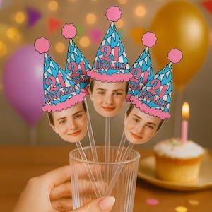 May include: A clear glass holds several party decorations. Each decoration features a face and a blue and pink party hat that reads "21 LEGALLY". A lit candle sits atop a cupcake in the background.