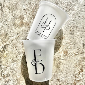 Może przedstawiać: Dwa białe plastikowe kubki z czarnym nadrukiem. G&oacute;rny kubek ma napis "Henry & Riley" i wz&oacute;r monogramu. Dolny kubek ma napis "E & D" i wz&oacute;r monogramu.