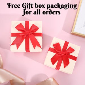 May include: Two white gift boxes with red ribbon bows. The boxes are on a pink background. The text "Free Gift box packaging for all orders" is at the top of the image.