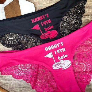 May include: Two pairs of black and pink lace underwear with the text "HARRY'S 19TH HOLE" and a golf ball graphic.