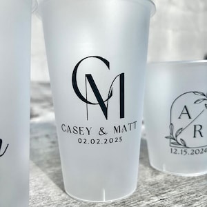 Może przedstawiać: Dwa matowe plastikowe kubki z czarnymi napisami. Pierwszy kubek ma inicjały "CM" i tekst "Casey & Matt 02.02.2025". Drugi kubek ma inicjały "AR" z kwiatowym wzorem i tekst "12.15.2024".