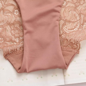 May include: A pair of pink underwear with delicate lace trim. The lace is a floral pattern and the underwear is made of a soft, stretchy fabric.