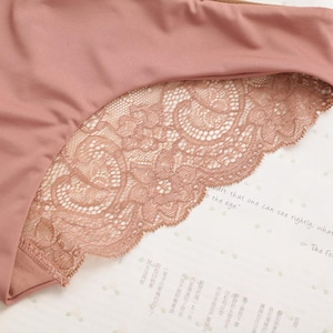 May include: A close-up of a pair of pink underwear with a lace trim. The lace is a delicate floral pattern and is a lighter shade of pink than the underwear.