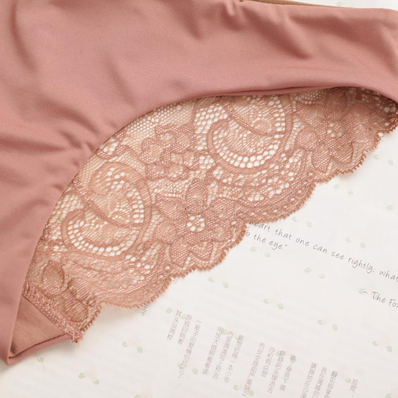 May include: A close-up of a pair of pink underwear with a lace trim. The lace is a delicate floral pattern and is a lighter shade of pink than the underwear.