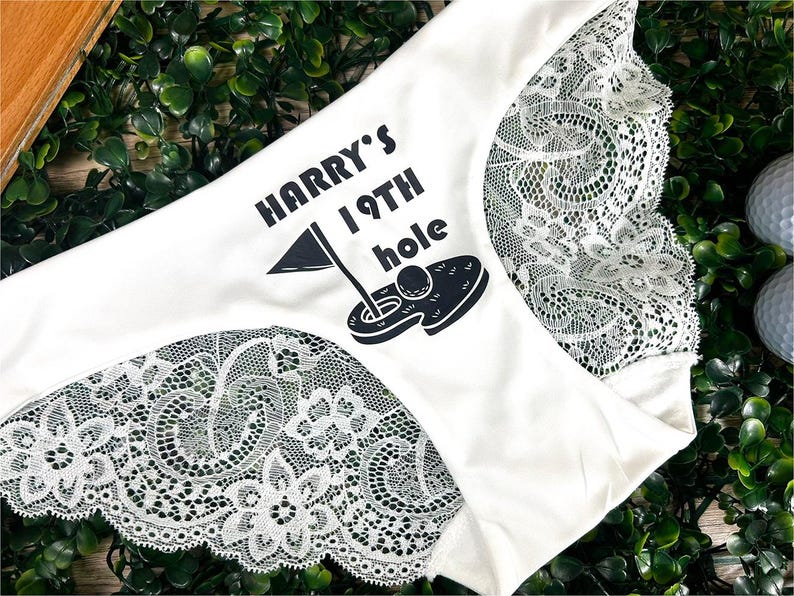 May include: White lace underwear with a black graphic print that says "Harry's 19th hole" and a golf ball in a hole.