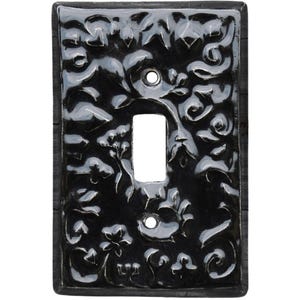 May include: Black decorative light switch cover with a floral design. The cover has a rectangular shape with a single switch opening and two screw holes. The floral pattern is painted in white and gray, creating a contrast against the black background.