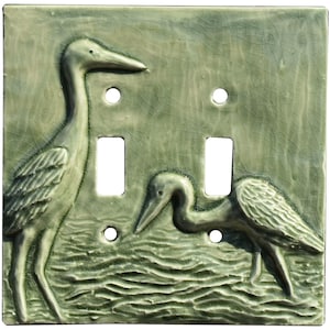 May include: A ceramic light switch cover with a green glaze features three sculpted heron birds in a watery scene.