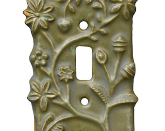 May include: A decorative, olive green ceramic light switch cover. The cover features an embossed floral design with flowers, leaves, and vines. The cover has a rectangular opening for the switch and two holes for mounting.