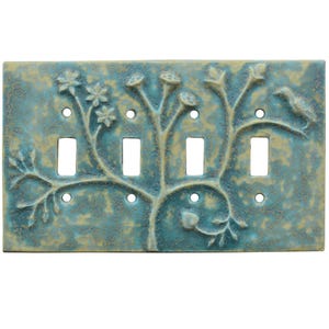 May include: A decorative four-gang light switch plate with a nature-inspired design. The plate has a textured teal and tan finish with an embossed tree, flowers, and a bird. It features four switch openings and small screw holes.