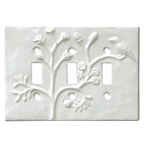 Puede incluir: Tapa de interruptor de luz de cerámica blanca con un diseño en relieve de un árbol estilizado con flores y un pájaro. La tapa del interruptor tiene tres interruptores de palanca.
