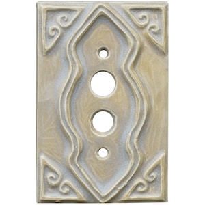 Może przedstawiać: Prostokątna, beżowa osłona włącznika światła z ozdobnym, symetrycznym wzorem. Osłona posiada trzy duże okrągłe otwory i jeden mały otwór, z dekoracyjnymi zawijasami w rogach i wzdłuż centralnego wzoru.
