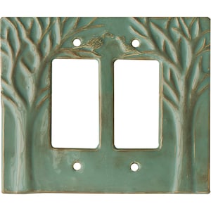 Puede incluir: Una placa de cubierta de interruptor doble de cerámica turquesa con un diseño de árbol y pájaros. La cubierta tiene dos aberturas rectangulares para los interruptores y cuatro orificios para tornillos. Las ramas de los árboles y los pájaros están en relieve.