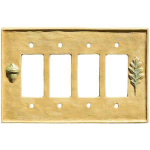 May include: A decorative light tan four-gang light switch cover with an acorn and leaf design. The cover has four rectangular openings for the switches and is made of a textured material.