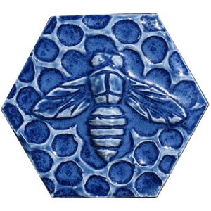 Puede incluir: Azulejo hexagonal de cerámica con diseño en relieve de abeja y panal. El azulejo es de color azul oscuro con detalles en azul claro, creando un efecto texturizado. La abeja está centrada en el azulejo.
