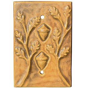 May include: A rectangular, bronze-colored wall plate with a raised relief design. The design features two acorns and oak branches with leaves. The plate has two circular holes, likely for mounting. The overall aesthetic is rustic and nature-inspired.