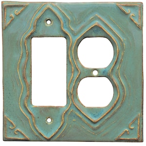 以下が含まれることがあります： 装飾的なデザインの正方形のターコイズセラミック製ライトスイッチカバー。ライトスイッチ用の長方形の開口部と、コンセント用の2つの円形の開口部があります。エッジとデザインの詳細は、ゴールデンブラウンの色で強調されています。