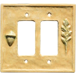 Peut inclure: Une plaque d'interrupteur double rectangulaire de couleur jaune clair avec une surface texturée. La plaque présente un relief de gland sur le côté gauche et un relief de feuille de chêne sur le côté droit, avec quatre trous de vis.