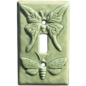 以下が含まれることがあります： 2つのエンボス加工された蝶のデザインが施された緑色のセラミック製ライトスイッチカバー。大きな蝶は上部に、小さな蝶は下部に配置されています。
