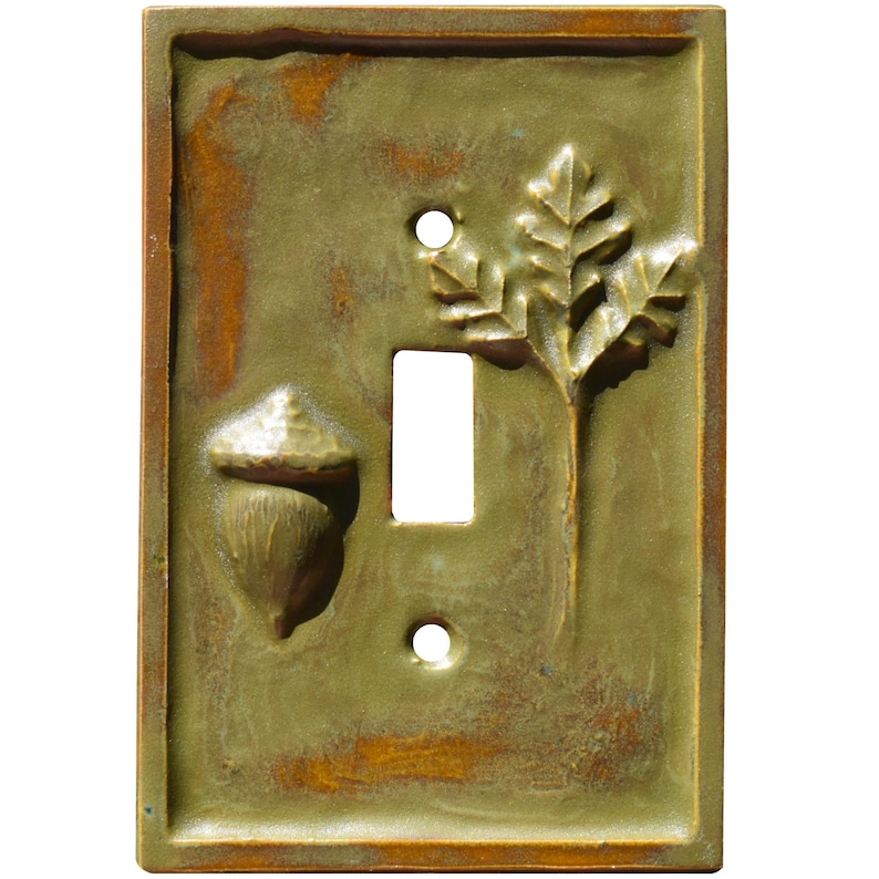 Puede incluir: Una tapa de interruptor de luz de cer&aacute;mica con un dise&ntilde;o de bellota y hoja de roble. La tapa es verde con acentos marrones.
