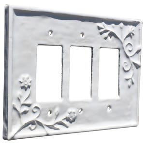 Puede incluir: Cubierta de cer&aacute;mica blanca para interruptor triple con dise&ntilde;o floral y de hojas en relieve. Tiene tres aberturas rectangulares para los interruptores y orificios para tornillos. Los bordes son ligeramente texturizados.