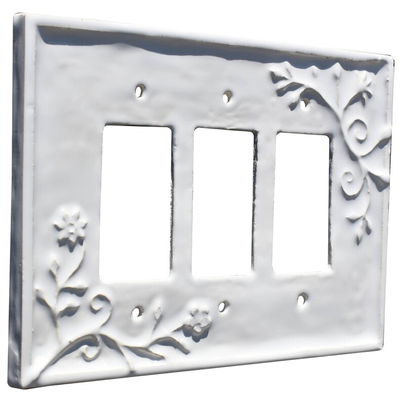 Puede incluir: Cubierta de cer&aacute;mica blanca para interruptor triple con dise&ntilde;o floral y de hojas en relieve. Tiene tres aberturas rectangulares para los interruptores y orificios para tornillos. Los bordes son ligeramente texturizados.