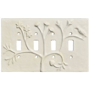 Puede incluir: Placa de interruptor de luz blanquecina con cuatro interruptores y un diseño en relieve. El diseño presenta un árbol estilizado con hojas, flores y un pájaro. Tiene cuatro aberturas para interruptores y orificios para tornillos.