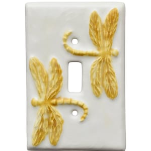 Puede incluir: Cubierta de interruptor de luz de cerámica blanca con dos diseños de libélulas doradas en relieve. Las libélulas tienen alas y cuerpos detallados. La cubierta tiene una abertura para un interruptor y dos orificios para tornillos. Medidas: aprox. 12 cm x 7 cm.