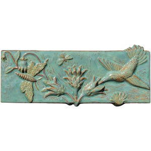 May include: A rectangular, turquoise ceramic tile with a relief design of a hummingbird, flowers, and insects. The hummingbird is in flight, and the flowers and insects are detailed with brown accents. The tile has a textured surface.