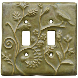 May include: A square, olive green double light switch plate featuring a raised, embossed relief design of botanical elements, including swirling vines, small flowers, and a bird perched on a branch, with four screw holes for mounting.