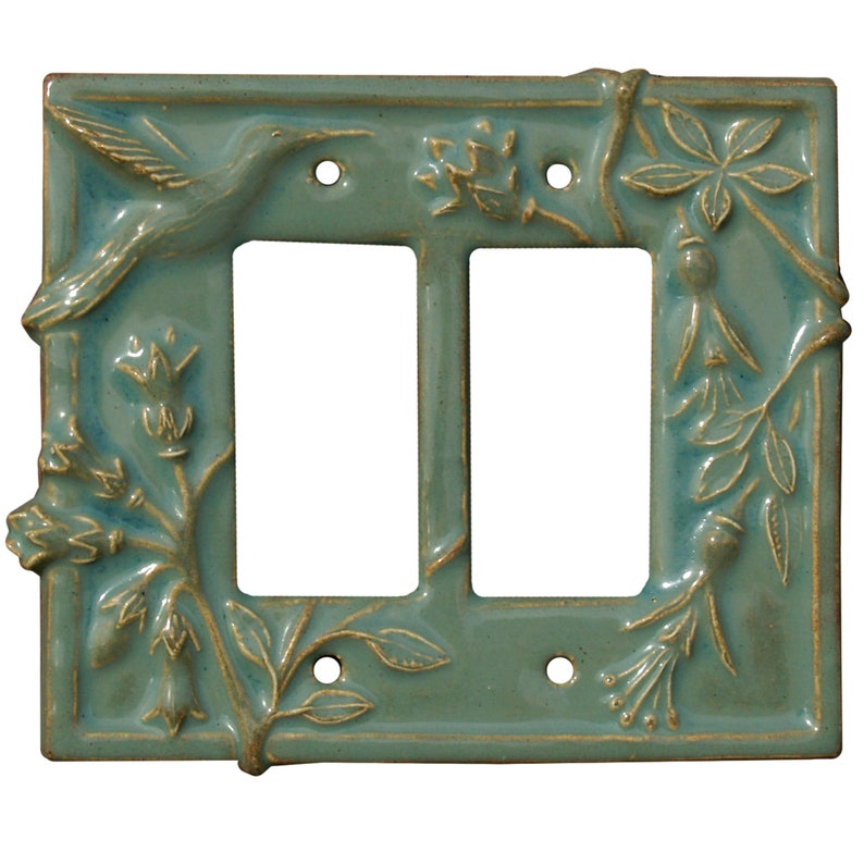 May include: A teal ceramic double light switch cover with a hummingbird and floral relief design. The rectangular cover has two openings for switches and four screw holes. The hummingbird is on the upper left corner, and floral elements are on the corners.