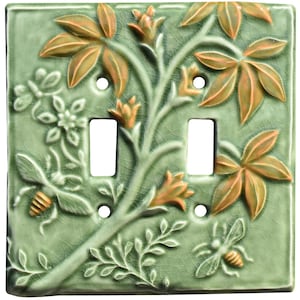 May include: A square double light switch plate featuring a raised relief design of a green vine with orange-tinted leaves, flowers, and two bees. The ceramic surface has a light green crackle glaze finish with four screw holes.
