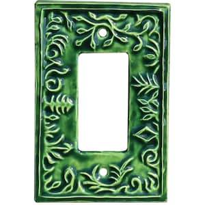 以下が含まれることがあります： 光沢のある緑色のセラミック製スイッチプレート。長方形の開口部があり、葉やツルをあしらった浮き彫りの植物模様で装飾されています。開口部の上下に2つのネジ穴が見えます。