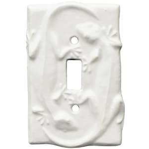 Könnte beinhalten: Weiße Keramik-Lichtschalterabdeckung mit einem erhabenen Reliefdesign von zwei Geckos. Die Geckos sind um die Schalteröffnung herum positioniert, mit detaillierten Texturen. Die Abdeckung hat zwei Schraubenlöcher und eine rechteckige Öffnung.