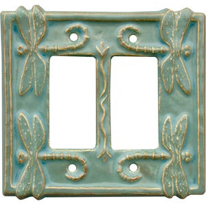 Może przedstawiać: Podw&oacute;jny przełącznik światła ceramiczny w jasnoniebieskim kolorze z wzorem ważki. Ważka jest w kolorze złotym, a przełącznik ma fakturowaną powierzchnię.