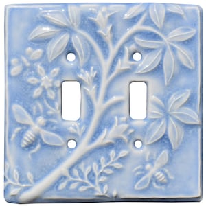 May include: A light blue ceramic double light switch cover with a white embossed design of a leafy branch with bees and flowers.