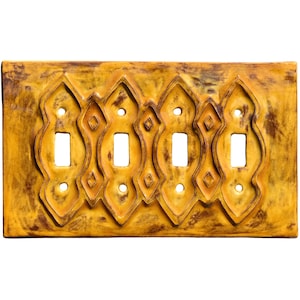 May include: A decorative light switch plate with four toggle switch openings. The plate is a warm, golden yellow with a textured surface and ornate, raised design elements. The design includes diamond and curved shapes.