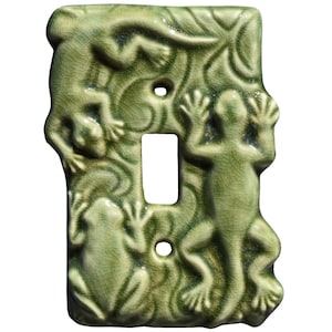 Puede incluir: Cubierta de cerámica verde para interruptor de luz con un diseño en relieve de ranas y lagartos. La cubierta tiene una abertura rectangular para el interruptor y dos orificios para tornillos. La superficie tiene un acabado craquelado.
