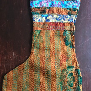 May include: A brown and gold Christmas stocking with a blue, green, and yellow patterned fabric trim. The stocking is made of kantha fabric, a traditional Indian textile.