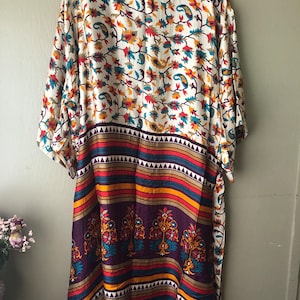 May include: A long, white kimono with a floral print and a colourful striped border. The kimono has a tie belt and is made of a soft, flowing fabric.