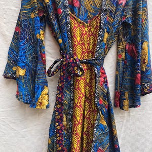 May include: A colorful, patterned robe with long sleeves and a tie waist. The robe features a mix of floral and abstract designs in blue, red, yellow, and white. The inner lining is a vibrant yellow and red leaf pattern.