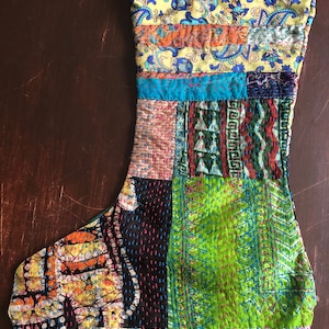 May include: A colorful patchwork Christmas stocking with a variety of patterns and textures, including paisley, geometric, and floral designs. The stocking is made of fabric scraps sewn together in a unique and eye-catching way.