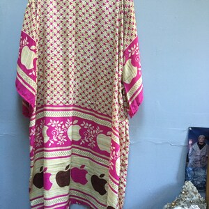May include: A long, pink and cream colored robe with a geometric pattern of pink triangles and a repeating pattern of brown apples with green leaves. The robe has a tie at the waist.