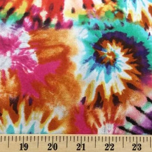 K&ouml;nnte beinhalten: Mehrfarbiger Batikstoff mit einem wirbelnden Muster in den Farben Rosa, Orange, Blau, Gr&uuml;n und Lila. Der Stoff wird mit einem Lineal in Zoll gemessen.