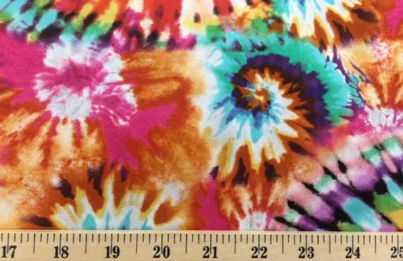 K&ouml;nnte beinhalten: Mehrfarbiger Batikstoff mit einem wirbelnden Muster in den Farben Rosa, Orange, Blau, Gr&uuml;n und Lila. Der Stoff wird mit einem Lineal in Zoll gemessen.