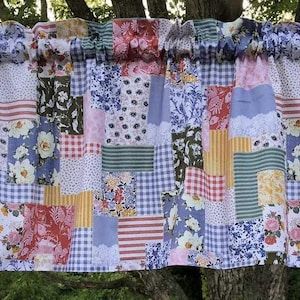 May include: A patchwork valance curtain featuring a variety of fabric squares in floral, gingham, and striped patterns with colors including pink, blue, yellow, and green. The curtain is gathered on a silver rod and displays the text Karen's Bed & Bath.