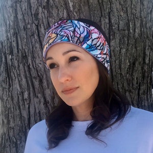 May include: A colorful headband with a stained glass design. The headband features a pattern of abstract shapes in shades of blue, orange, purple, and white, outlined in black. The headband is worn by a person.