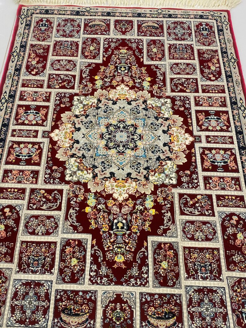 May include: A detailed, rectangular rug with a central medallion and repeating floral patterns. The rug features a deep red background with cream and blue accents. The design includes floral motifs and geometric borders, creating a traditional aesthetic.